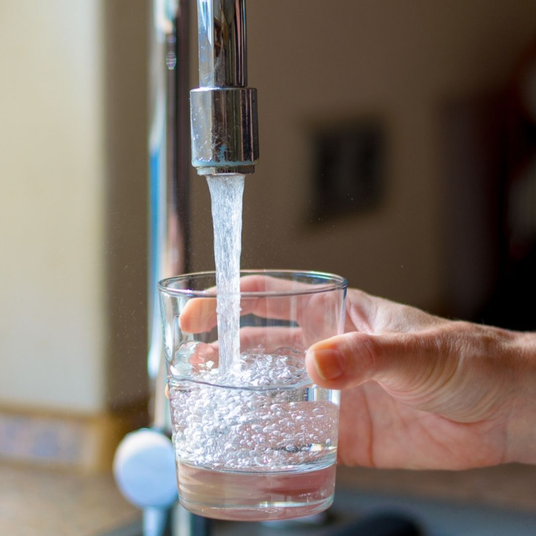 A homeowner filling up a glass of water from their kitchen faucet