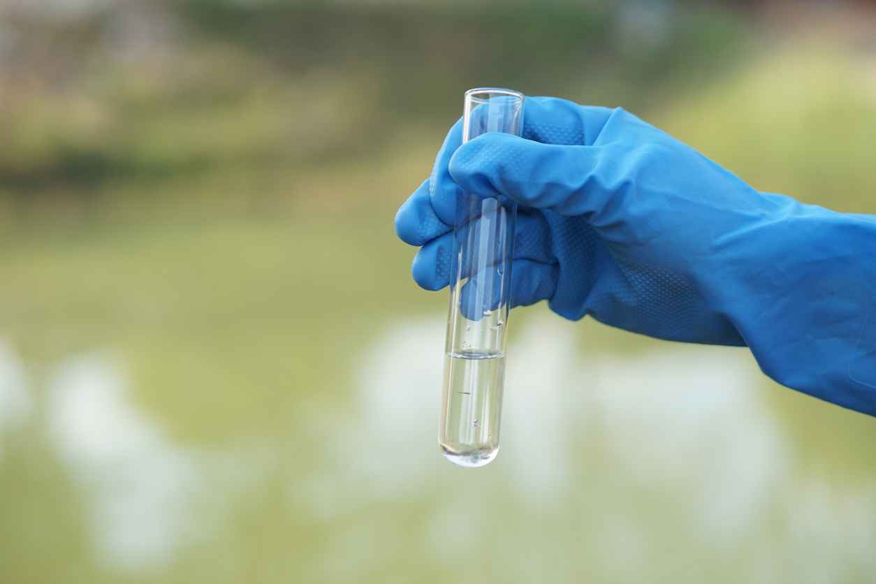 Close up scientist hand hold glass tube that contains sample of water to do science experiment. Concept Testing of water quality and contaminants from natural water sources